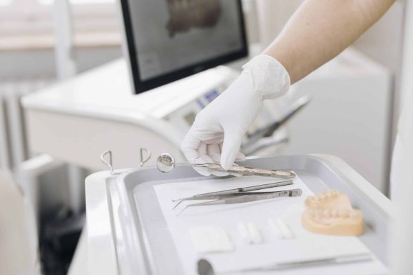 Eine Hand im Handschuh nimmt ein zahnmedizinisches Instrument | Zahnarztpraxis Dr. Stefan Bernuth in Würzburg