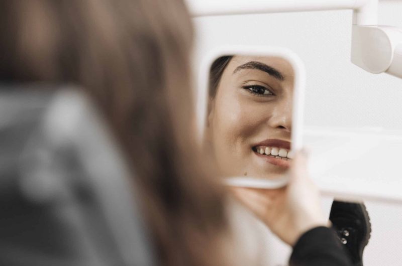 Eine Frau betrachtet sich im Spiegel in der Zahnarztpraxis Dr. Stefan Bernuth.