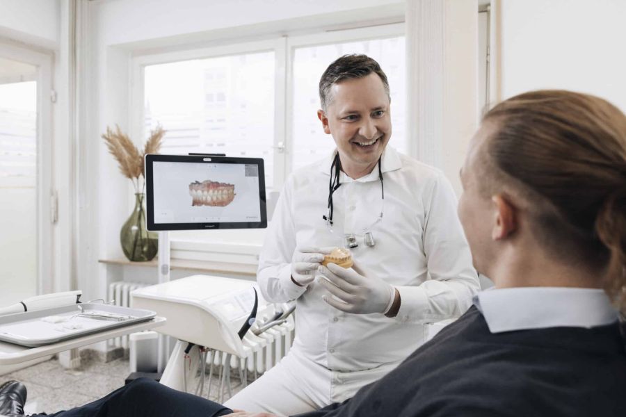 Dr. Stefan Bernuth erklärt einem Patienten etwas zu einem 3D-Zahnmodell